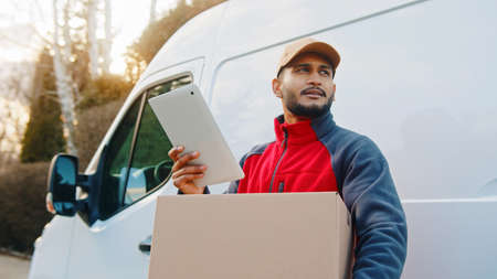 Adult logistic worker waiting at van for client to deliver parcel. Man looking away. Using modern wireless technology at work.の写真素材