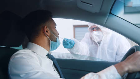 Drive-in  testing place. Person in protective equipment collecting sample through open car window....