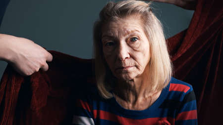 Young person covering his grandmother with red blanket. Care of elderly people in nursing home. High quality photoの写真素材