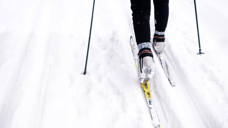 Cropped view of legs and skis while sporting. Back view on ski runner on track. Hobby cross country...