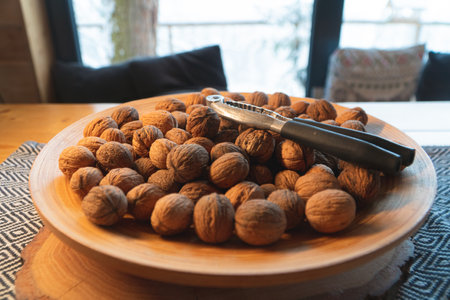 Closeup view of a bunch of walnuts on a white plate with a metallic nut cutter. The plate is placed...
