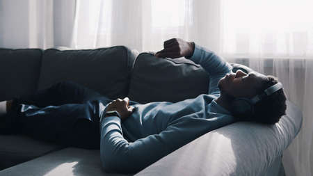 African American man wearing headphones listening to music. Lying on The Couch. High quality photoの写真素材