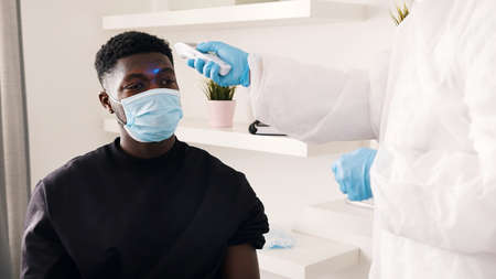 Nurse uses thermometer to take temperature of young african american black man. High quality photoの写真素材