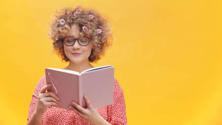 Young caucasian woman with glasses and flowers in curly hair reading a book. Spring concept. High quality photoの写真素材