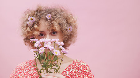Beautiful young caucasian woman with bouquet of spring flowers over her face and floral decoration...