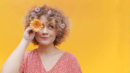 Playful young woman with curly hair holding flower over her eye. High quality photoの写真素材