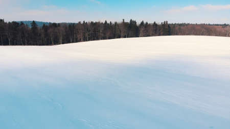 Snow-covered sloppy landscape during the winter season. Grove of trees in the background. Bright...