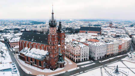 Aerial view of the Krakowâs Rynek GÅowny (Central Square) surrounded by historic buildings. Twin towers of the Basilica of Saint Mary against clear white sky in the background. City Skyline.の写真素材