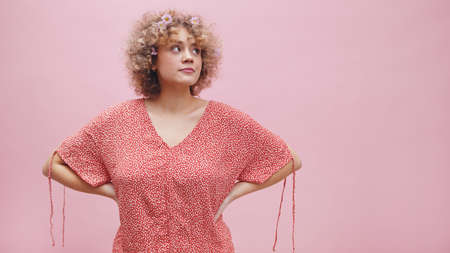 Attractive young girl standing with hands on waist looking away from the camera. Isolated on pink...