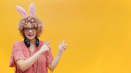Excited young girl wearing bunny ears and glasses pointing at something. Girl in joyful mood....
