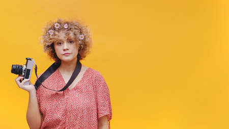 Attractive young photographer isolated on bright yellow background studio. Camera hanging from her...