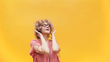 Beautiful girl listening to music on her headphones. Girl in a good mood wearing round spectacles and enjoying her favorite music. Isolated on bright yellow background. Music Lover. Enjoyment.の写真素材