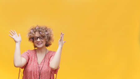 Beautiful girl enjoying her favorite music through her headphones. Girl in a good mood wearing round spectacles and enjoying with eyes closed. Isolated on bright yellow background. Music Lover.の写真素材