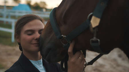 Horsewoman touching her face to the seal brown horse. Holding its bridle expressing her love for the...