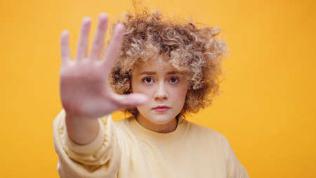 Girl making stop hand gesture. Serious young girl making a stop sign with her hand. Dressed in a...