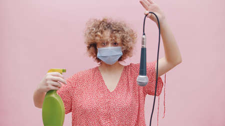 Girl wearing a face mask and a green spray bottle in her hand. Holding a mic upside down with its wire. Disinfecting the mic with disinfectant. Concept of sanitizing. Covid 19. Following Sops.の写真素材