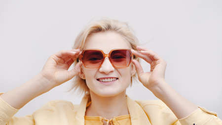 Carefree girl wearing sunglasses. Isolated girl over white background studio. The girl is dressed in a yellow jacket and posing for the camera touching her glasses. Vacations concept.の写真素材