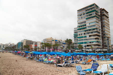 Benidorm, Spain 18.08.2021 Sunbathing chairs and Umbrellas at the Benidorm beach Mediterranean of Spain. High-rise building against the clear white sky in the background. Famous tourist spot.のeditorial素材