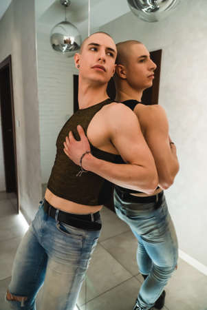 European queer lgbt person in black tank top and jeans posing indoors next to the mirror . High...
