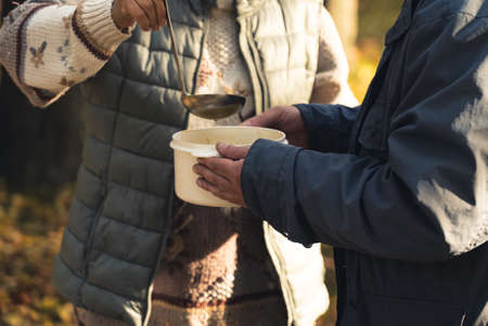 White cooking pot with warm soup held by a volunteer, giving food for homeless people in need. Vertical Outdoor Shot. High quality photoの写真素材