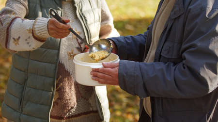 Elderly caucasian person shares her homemade soup to help the unemployed people in need. High quality photoの写真素材