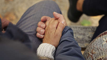 Caucasian elderly couple holding their old, wrinkled hands together while sitting on a bench. High quality photoの写真素材