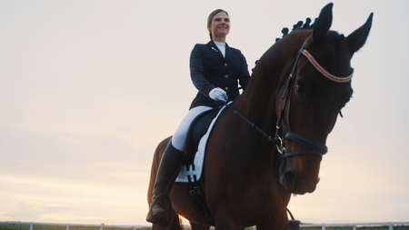 a beautifully trained smiling young woman rides a horse with her head bowed. High-quality photoの写真素材