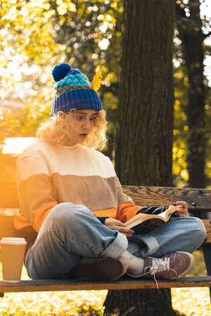 surprised young millennial girl reading book on bench in park - medium shot. High quality photoの写真素材