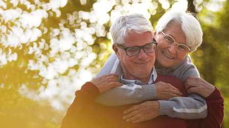 Portrait of happy elderly Caucasian couple woman hugs her husband from the back both smiling man...