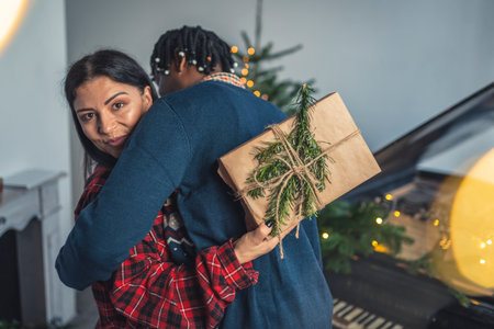 Interracial couple celebrating Christmas. Embrace between two spouses. Caucasian woman showing present to the camera. High quality photoの写真素材