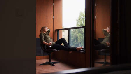 Full shot of a middle-aged caucasian woman sitting on a chair on her balcony with a glass of wine...