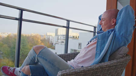 Caucasian queer gay sitting in an armchair on balcony, smiling, and being content with his life....