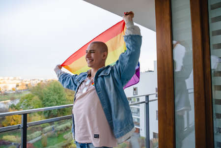 Proud non-binary queer person holding rainbow pride flag and smiling. Medium close up shot. High quality photoの写真素材