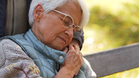Portrait of aged Caucasian woman with glasses holding hand of her husband and closing eyes copy space park background . High quality photoの写真素材