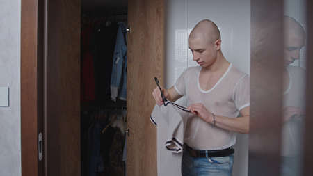 Fashionable caucasian gay man in a white mesh t-shirt cleaning in his closet, looking at his t-shirts. High quality photoの写真素材
