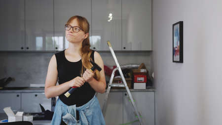 Middle-aged European red-haired woman holding a hammer and thinking about her next renovation project. High quality photoの写真素材