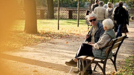 Senior Caucasian couple sitting on the bench in the park, disabled husband in glasses and a stick park selective focus full shot copy space . High quality photoの写真素材