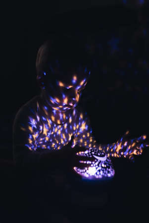 Ball projecting colorful shapes light on child. Vertical indoor shot. High quality photoの写真素材