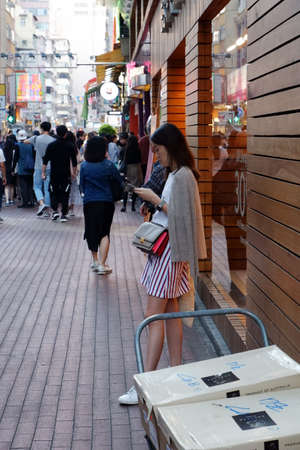 Hong Kong street scene with a young girl waiting on her phone in Mongkok Kowloon.のeditorial素材