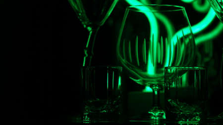 Glasses and shots highlighted by green light on a black background. Low key.の写真素材