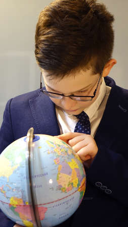 Schoolboy in glasses with a globe in his hands on a gray glass surface background. Back to school. Concept of school and pre-school education and learning.の写真素材