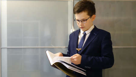 School boy in eyegasses is holding a book and turn on the pages.