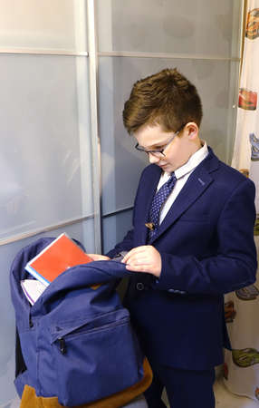 Boy in school uniform and eyeglasses collects a bag for schoolの写真素材