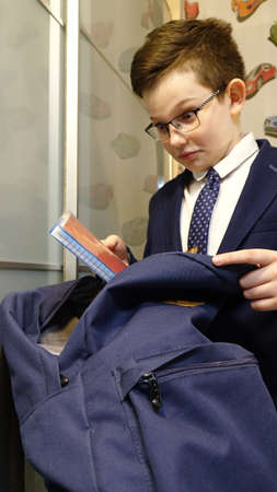 Boy in school uniform and eyeglasses collects a bag for schoolの写真素材