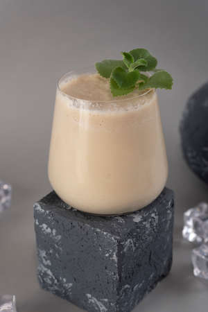 Glass of traditional Indian lassi drink with mint leaf and mango on a grey background. Vertical...
