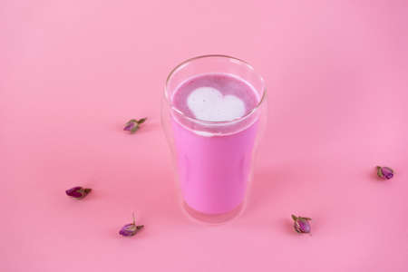 Pink rose milk with rose petals. Heart-shaped foam in a glass of moon milk. Healthy drink. Side view.の写真素材