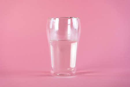 Glass of fresh pure water in a double walled glass on pink background. Side view.の写真素材