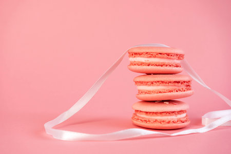 Delicious pink macaroon cookies with white ribbon on a pink background. A great idea for a holiday gift.の写真素材