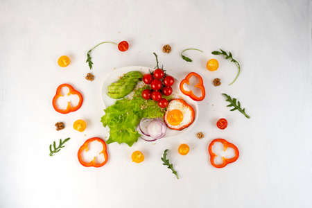 Delicious family breakfast with fried scrambled egg, avocado, cherry tomatoes, onion rings, bell peppers and salad on white plate.の写真素材