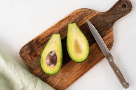Chef cuts fresh avocado in half on a cutting board with a knife. Vegetarian food.